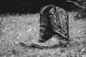 Artistic black and white photo of vintage cowboy boots resting on grassy ground.